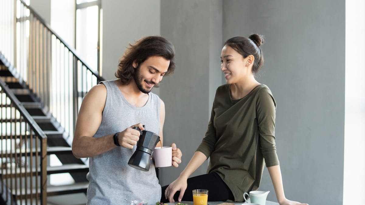 A couple enjoy a casual breakfast indoors with coffee and food, smiling and relaxed.